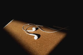 White earphones placed on a wooden surface, illuminated by a spotlight, with a dark shadow surrounding the focal point.