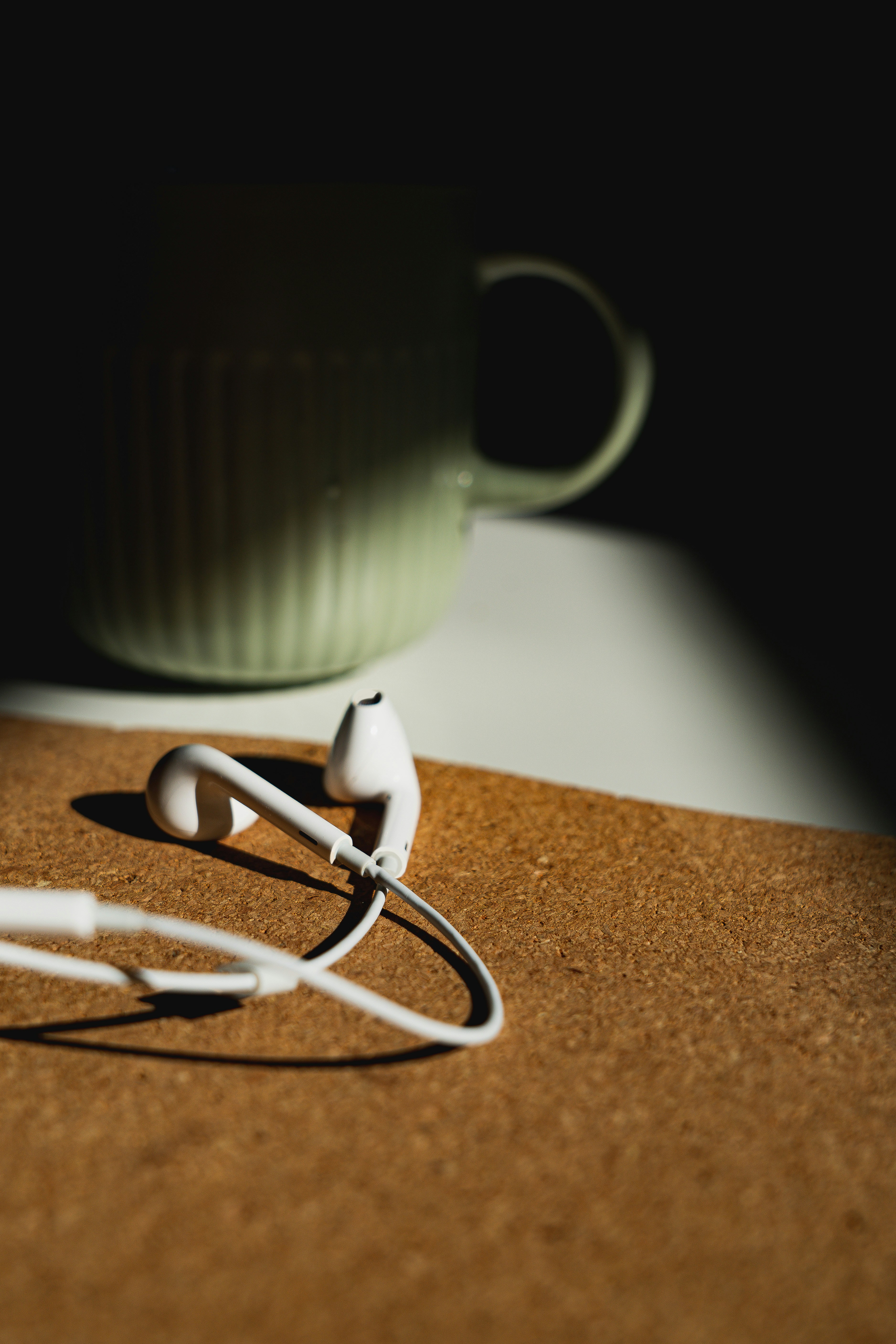 white Apple EarPods beside white ceramic mug