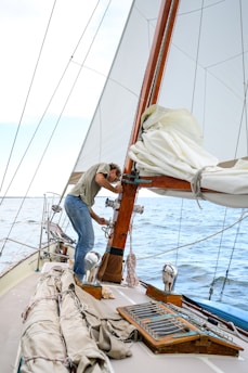 man in gray shirt and blue denim jeans sitting on white and brown sailboat during daytime