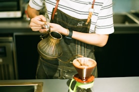 woman pouring brown liquid on clear glass mug