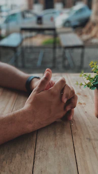 A close-up of supportive hands joined together over a wooden table with natural decor.