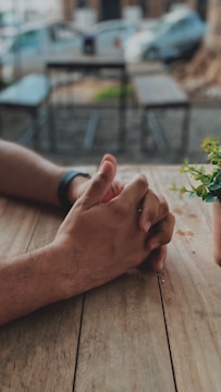 Hands joined together in support over a wooden table.