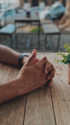 Close-up of intertwined hands resting on a rustic wooden table