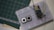 A breadboard setup featuring an electronic circuit. Two tactile push buttons and an ESP8266 module are connected with several jumper wires. The breadboard rests on a surface with a green cutting mat and a notepad visible in the background.