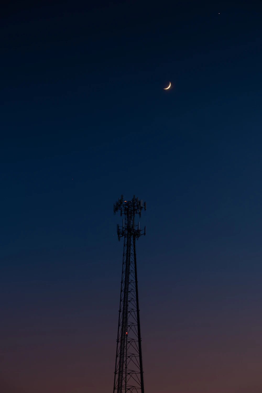 A small tower silhouette under a deep blue night sky with a crescent moon