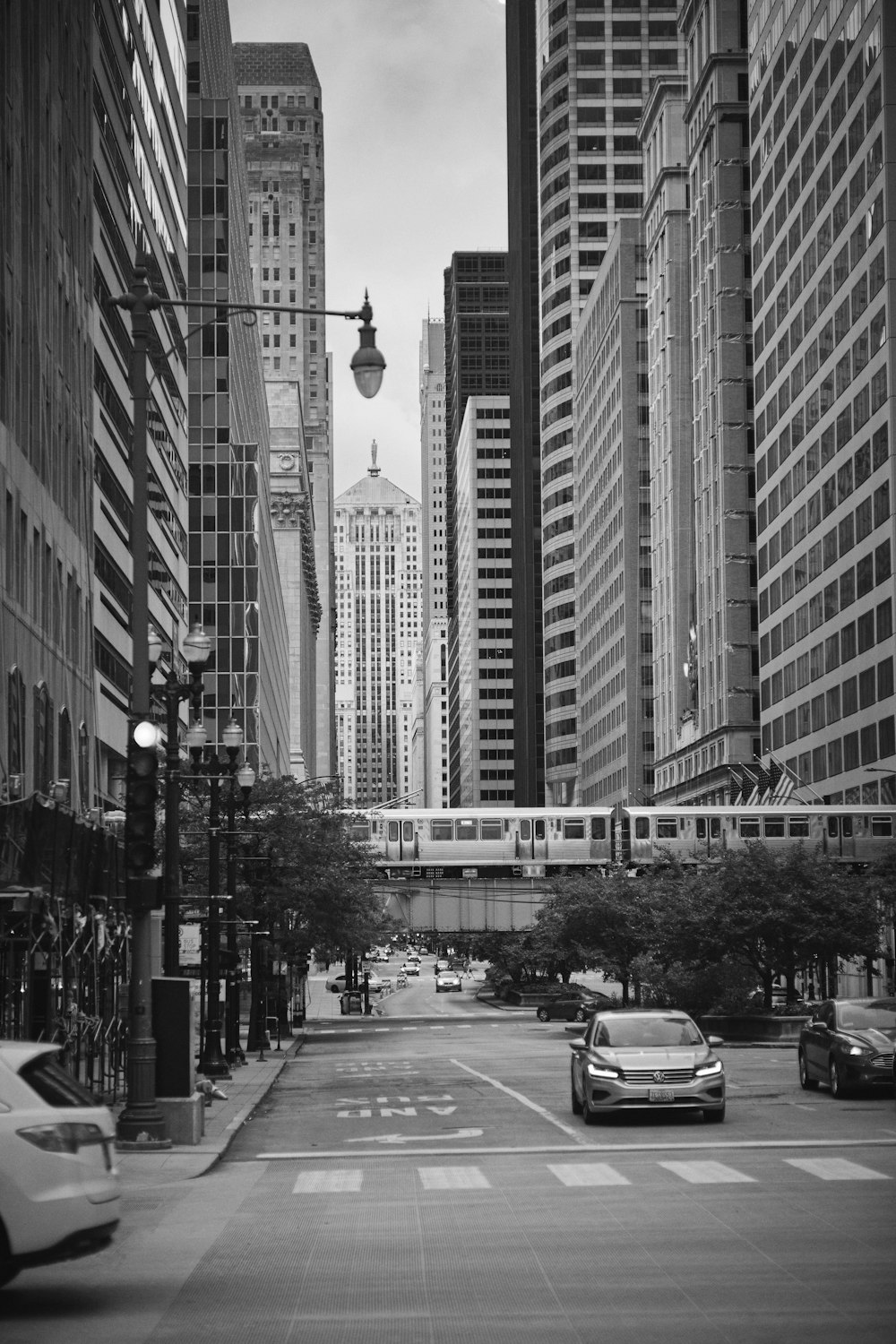 grayscale photo of cars on road between high rise buildings