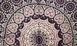 Intricate mandala pattern featuring a series of concentric circles adorned with floral and paisley motifs. The design includes heart-shaped elements filled with detailed floral patterns, primarily in shades of red, black, and white. The symmetry and repetition create a sense of balance and harmony.