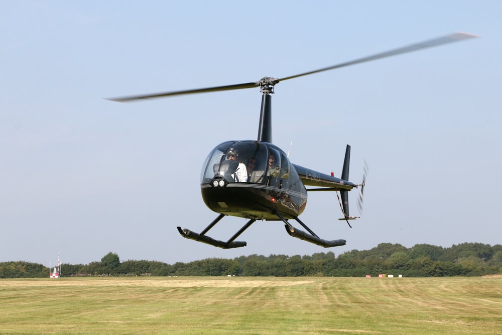 black helicopter flying over green grass field during daytime