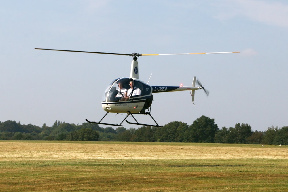 white and black helicopter flying over green grass field during daytime