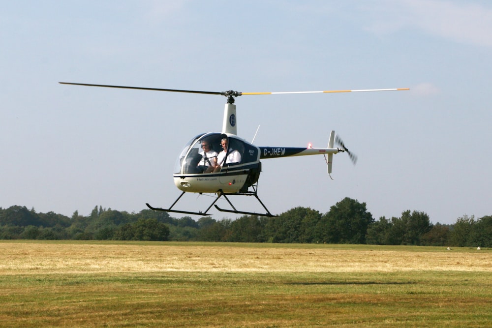 weißer und schwarzer Hubschrauber, der tagsüber über grünes Grasfeld fliegt