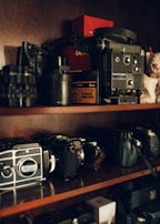 A collection of vintage camcorders and photo frames on a rustic wooden shelf.