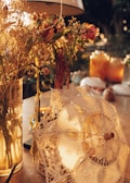 A delicate lace parasol rests gently on a table, surrounded by a warm and cozy ambiance. Soft sunlight filters through, highlighting a bouquet of dried flowers and a few glowing candles that add a touch of tranquility and charm.