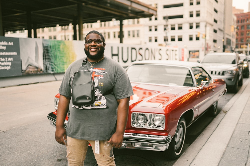 man in gray crew neck t-shirt standing beside red car during daytime