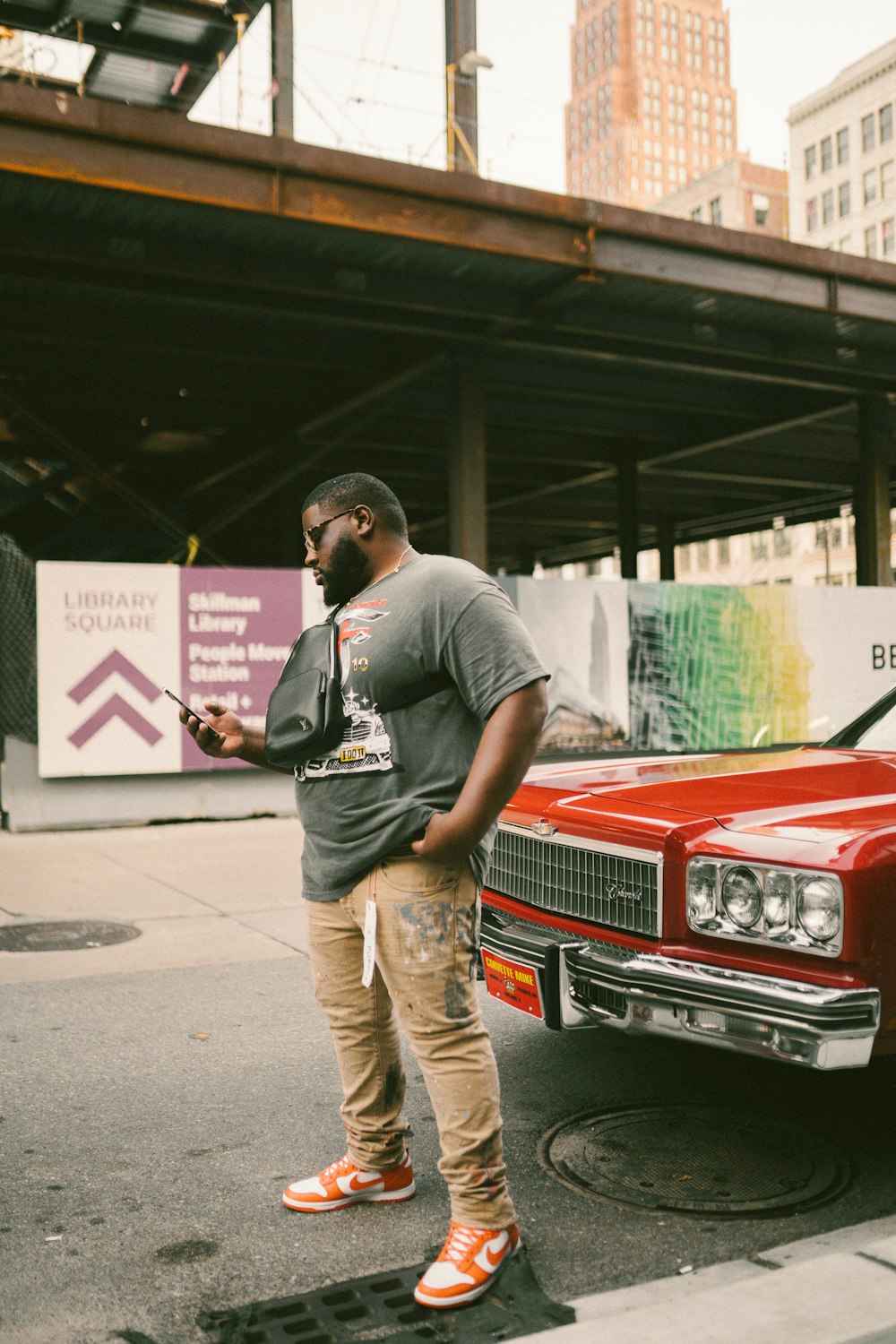 man in grey t-shirt and brown pants standing beside red car