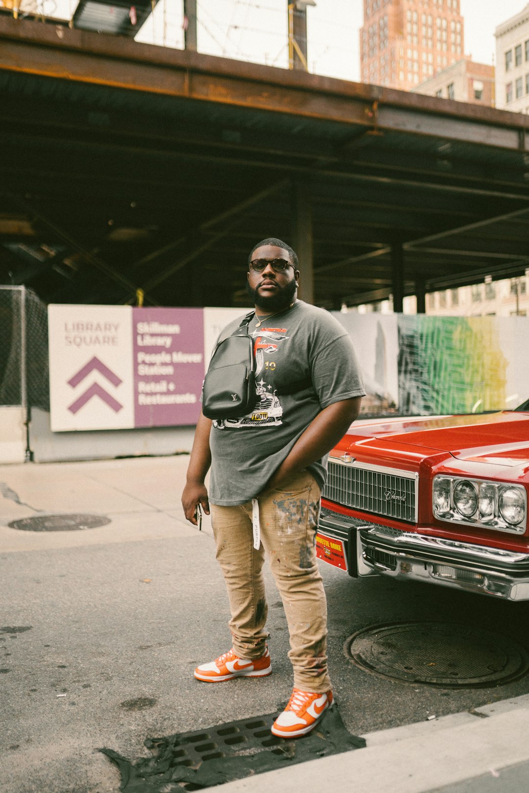 man in gray crew neck t-shirt and beige pants standing beside red car