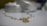 A delicate bracelet featuring pearls and gold links is placed on a smooth surface. The focus is on the jewelry, with cylindrical shapes and a metal pendant creating a luxurious feel. The background is softly blurred, highlighting the elegance of the piece.