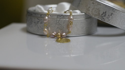 A joyful young woman wearing layered bracelets, smiling as she opens a naje jewelry box with a bright background.