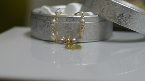 An elegant, decorative bracelet with pearls and a gold charm is draped over an ornate silver box, which has a floral pattern. The box lid is slightly ajar, revealing a soft, white interior.