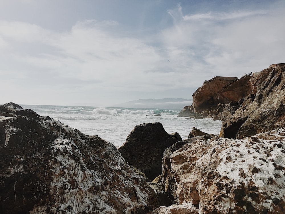 brown rock formation on sea under white clouds during daytime