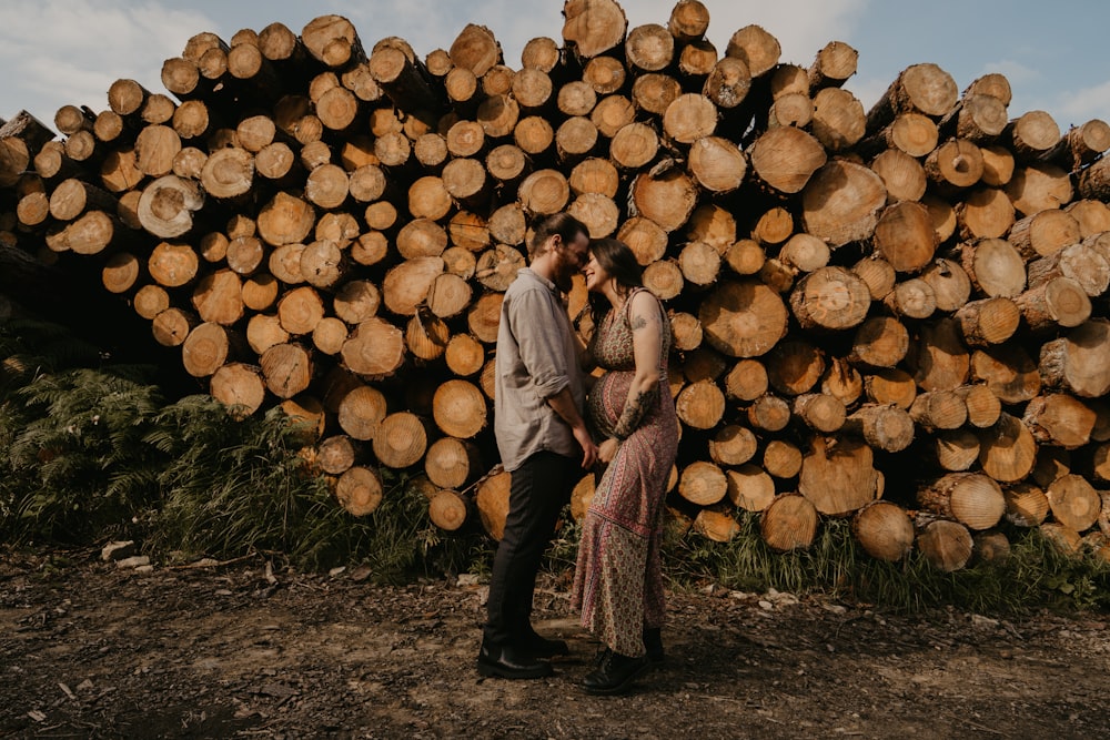 man and woman standing beside brown wood logs