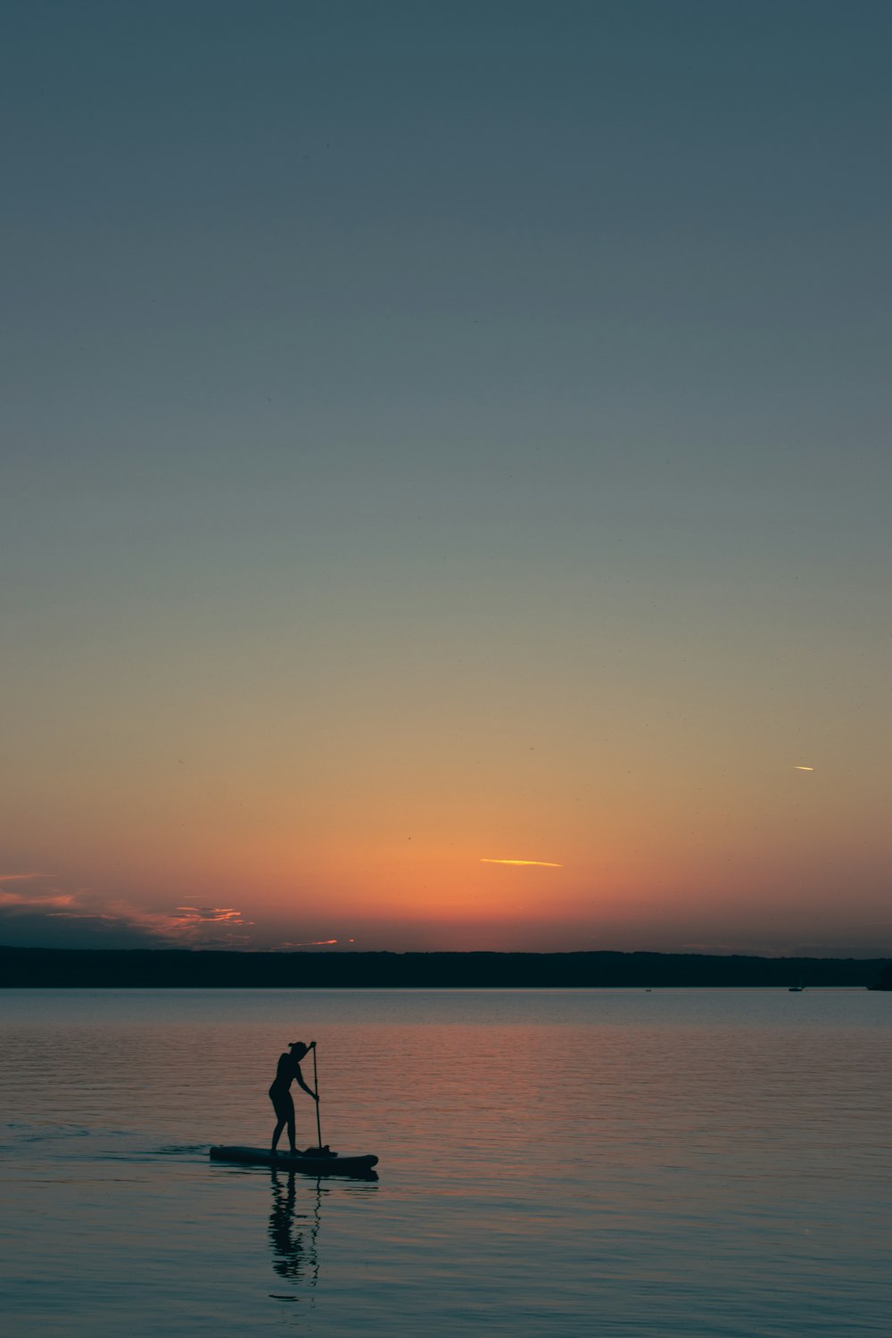 silhouette of person standing on sea shore during sunset