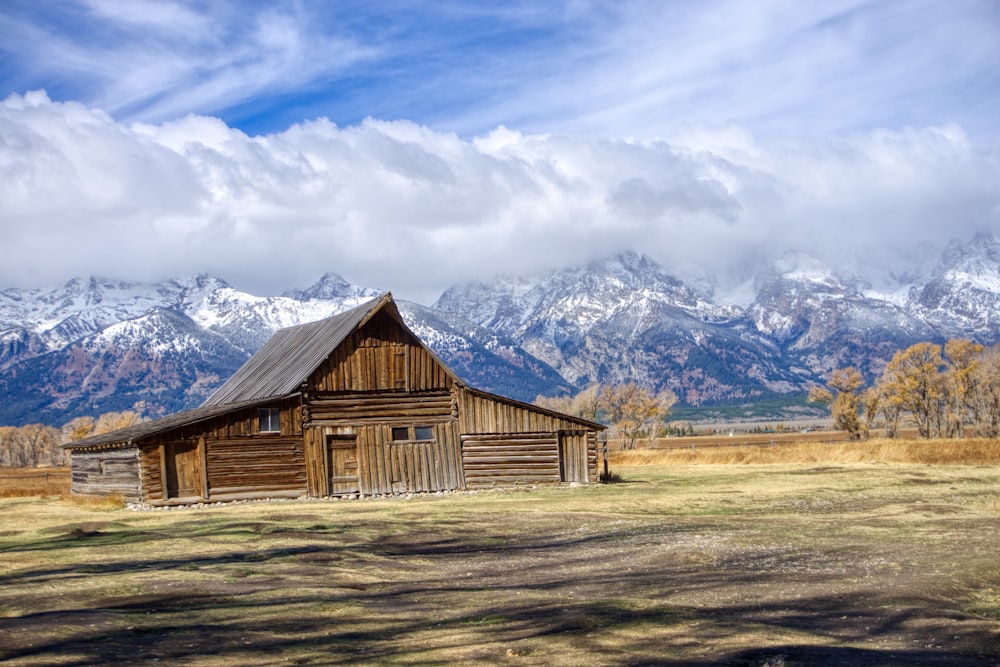Braunes Holzhaus auf braunem Grasfeld in der Nähe eines schneebedeckten Berges tagsüber