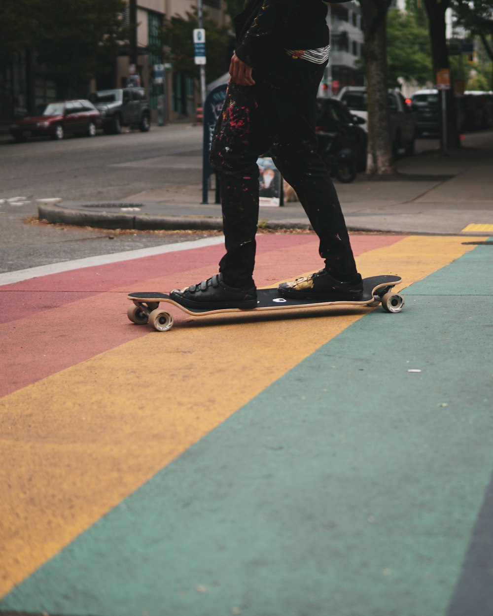 Mann in schwarzen Hosen und schwarzen Schuhen, der tagsüber auf dem Skateboard fährt