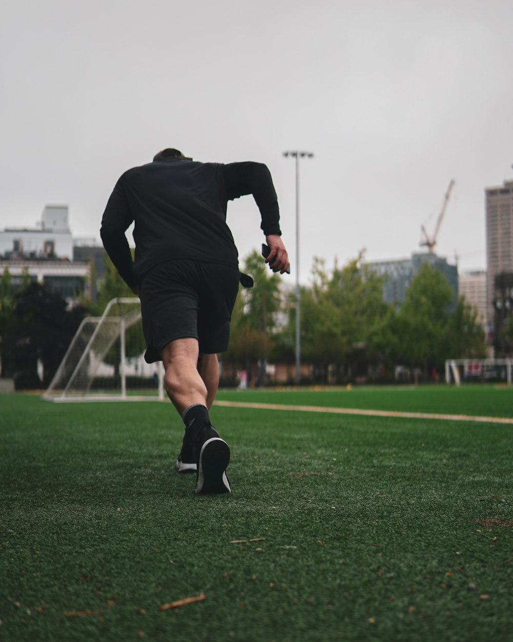 man in black long sleeve shirt and black shorts running on green grass field during daytime