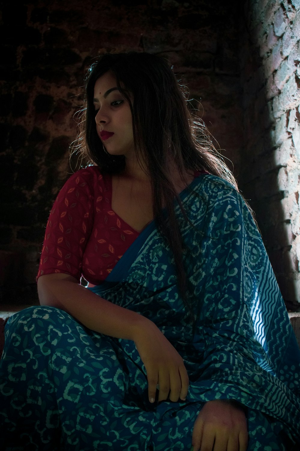 woman in red long sleeve shirt and blue and white floral pants sitting on brown concrete