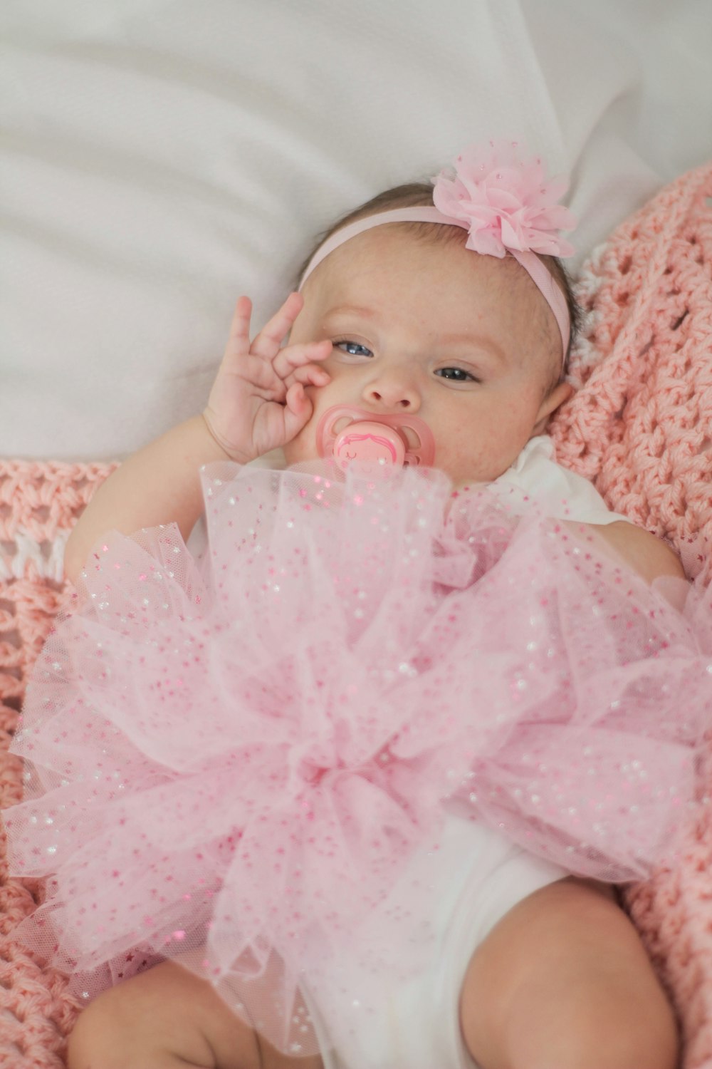 baby in pink and white floral dress lying on white textile