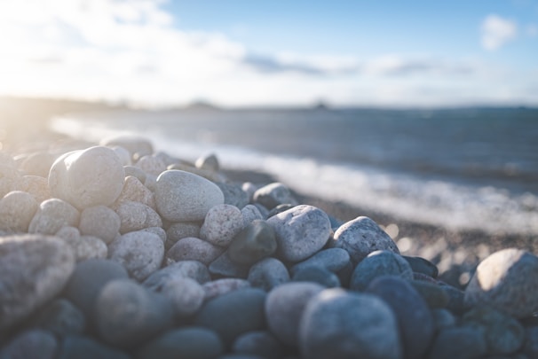 Close-up of smooth spa stones stacked on a sand-colored towel with gentle ocean waves blurred in the background.