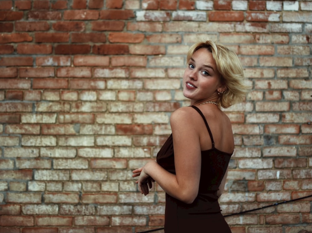 woman in black spaghetti strap dress standing beside brown brick wall