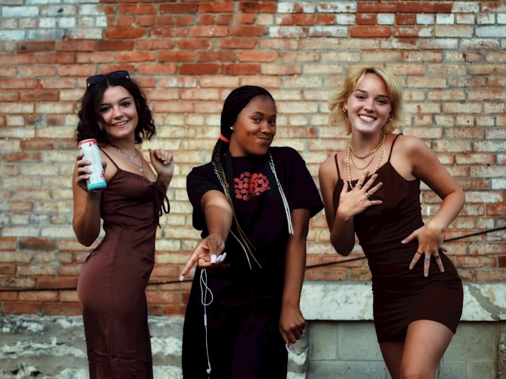 2 women in black tank top standing beside brown brick wall