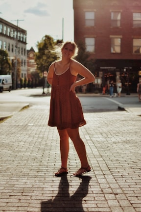Elegant woman in a flowing terracotta dress standing on a sunlit Salvador street.