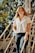 woman in white button up shirt and blue denim jeans sitting on brown wooden bridge during