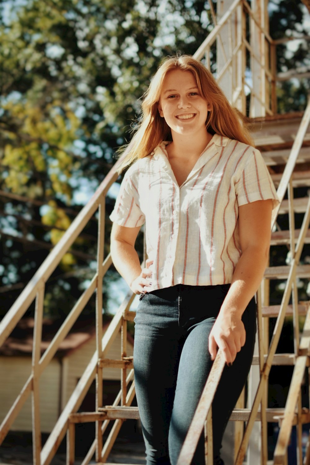 woman in white button up shirt and blue denim jeans sitting on brown wooden bridge during