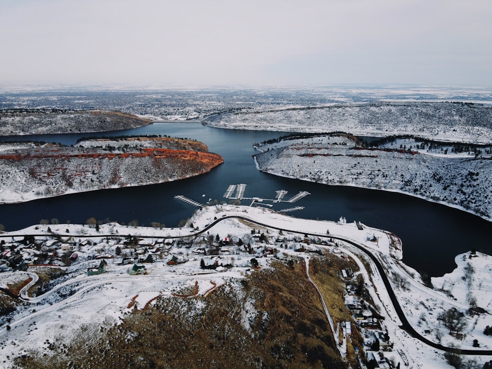Vista aérea de un campo cubierto de nieve y árboles cerca del cuerpo de agua durante el día