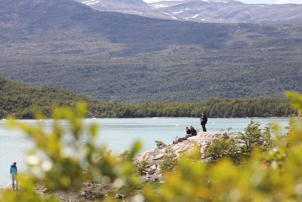 people sitting on rock near lake during daytime