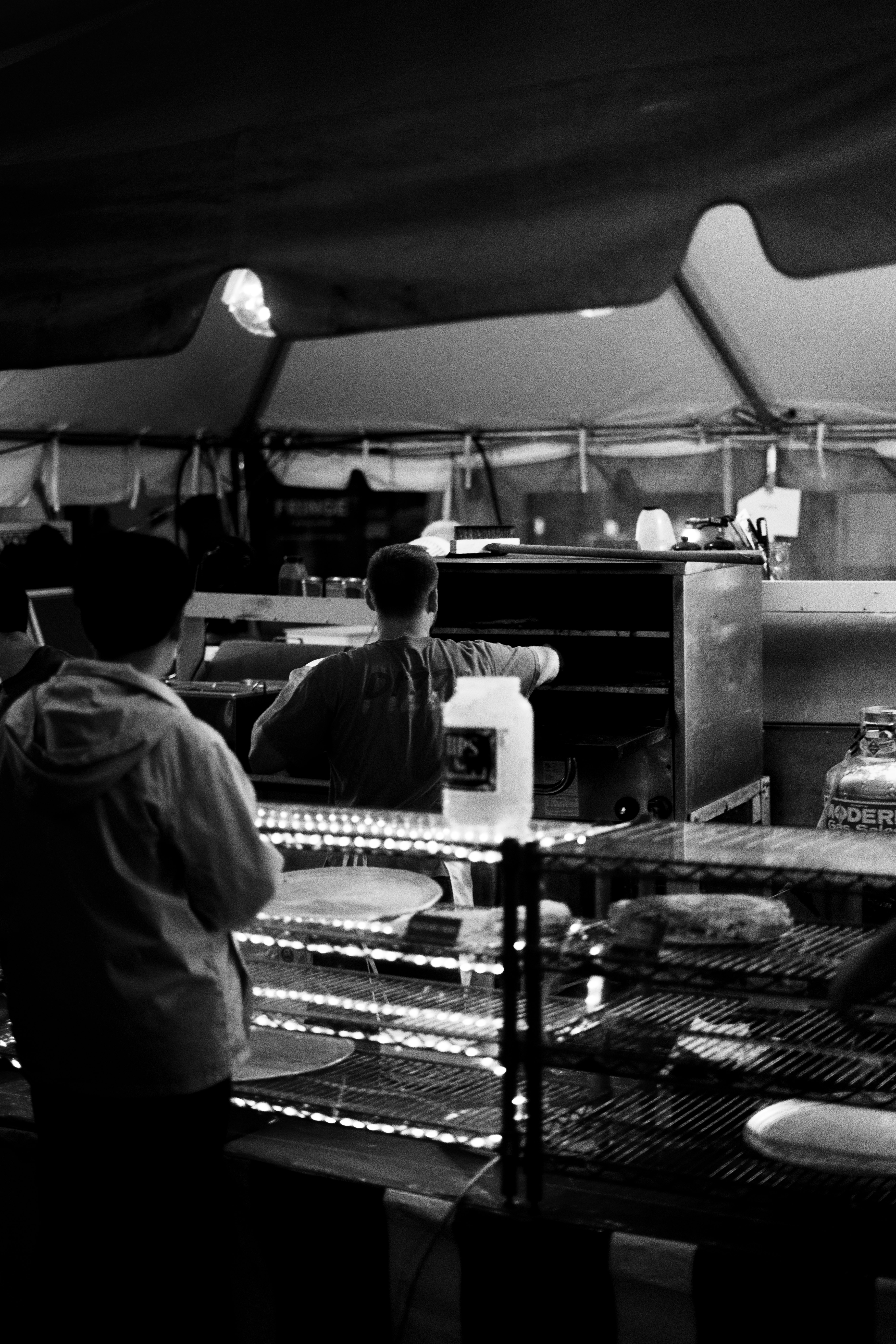 grayscale photo of man in white dress shirt standing in front of food cart