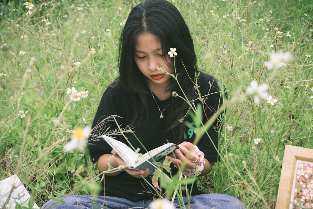 黒いシャツとブルーデニムのジーンズを着た女性が緑の芝生に座って本を読んでいます