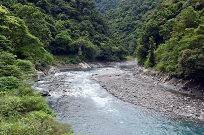 Serene riverside beach on the Chillón River surrounded by mountains and greenery.