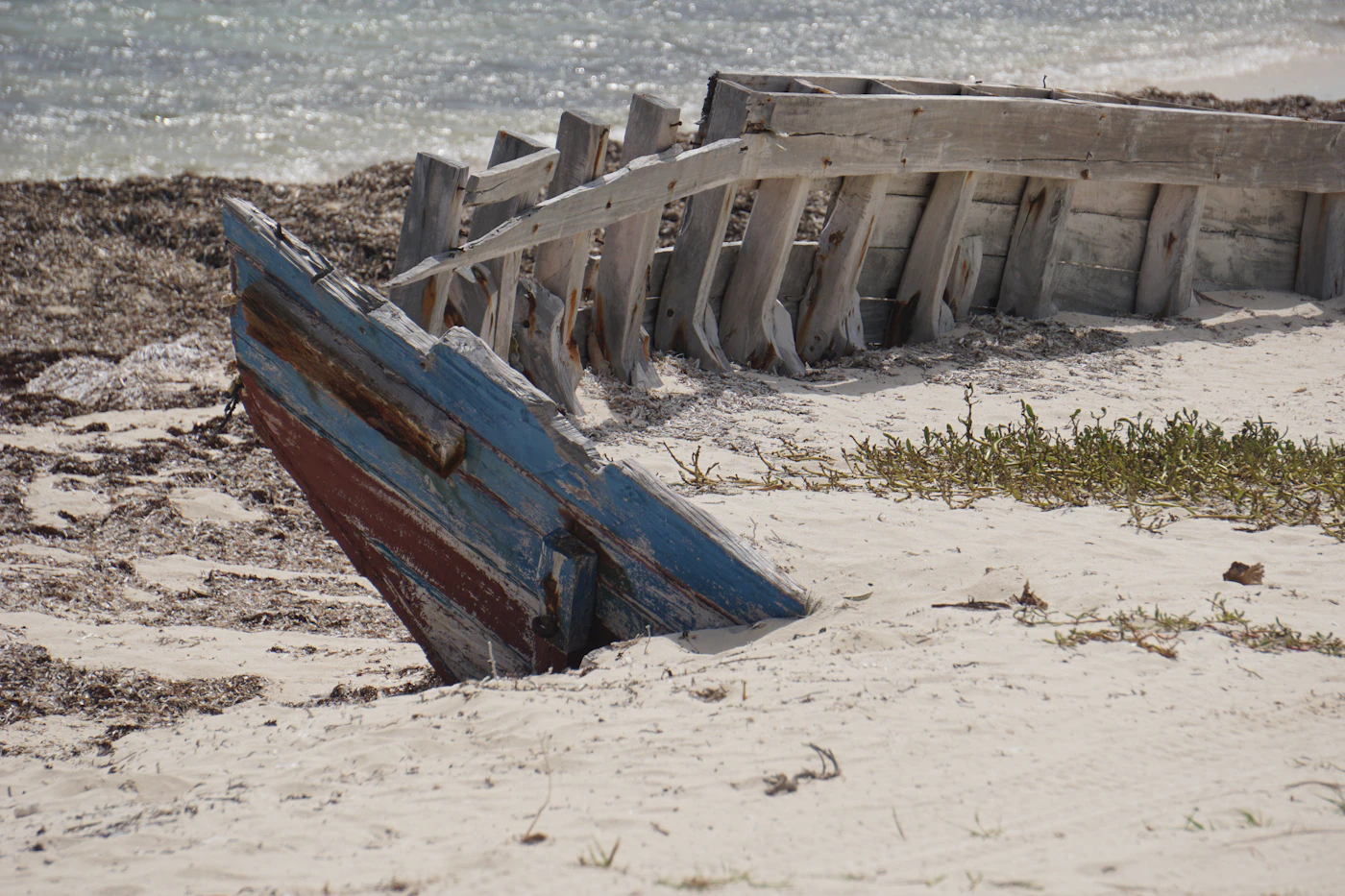 A traditional wooden boat resting on the white sand of a Turks and Caicos beach with the turquoise water and blue sky behind it