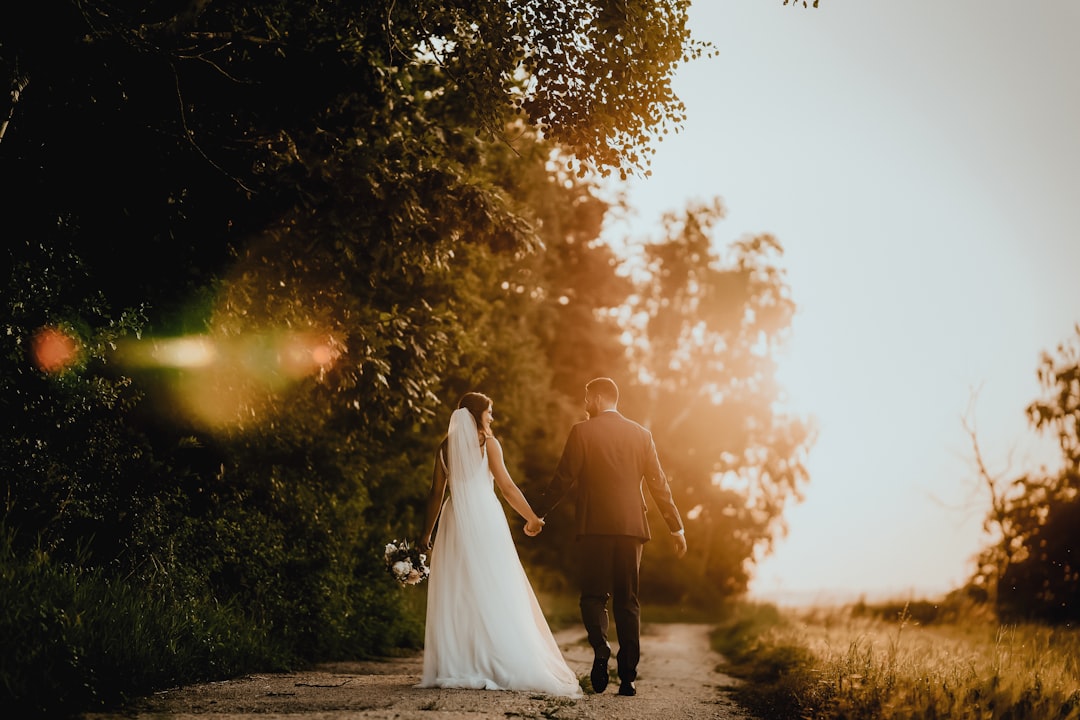 man and woman walking on pathway between trees during sunset