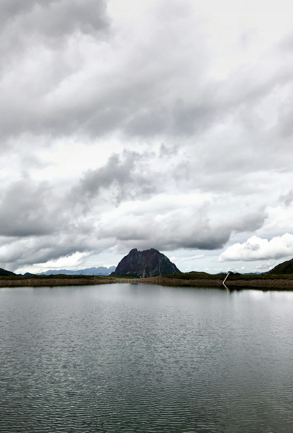 body of water near mountain under white clouds during daytime