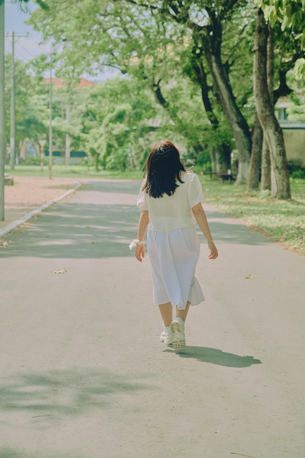 Mujer en vestido blanco caminando en camino de asfalto gris durante el día