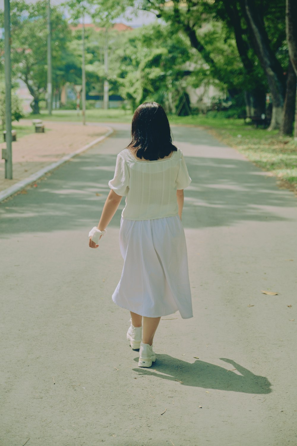 Muchacha en vestido blanco caminando en camino de asfalto gris durante el día