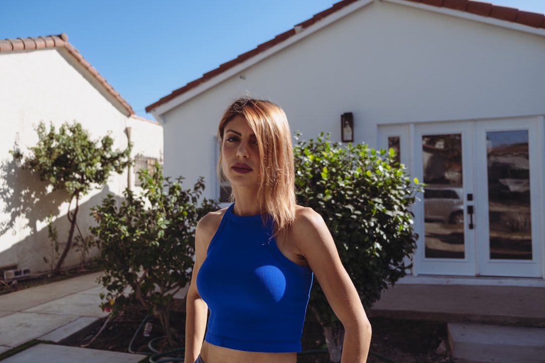 woman in blue tank top standing near white house during daytime