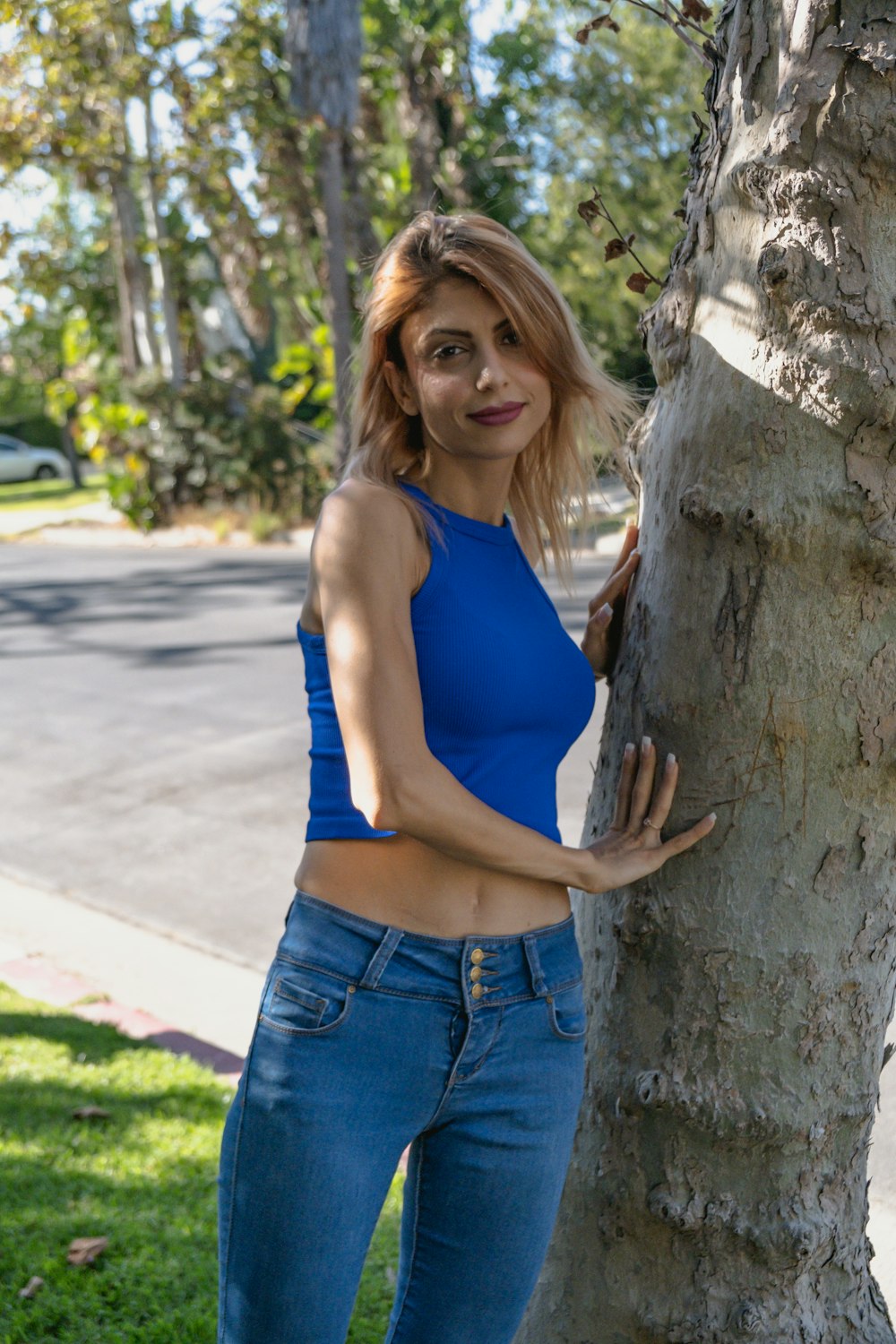 woman in blue tank top and blue denim shorts leaning on brown tree trunk during daytime