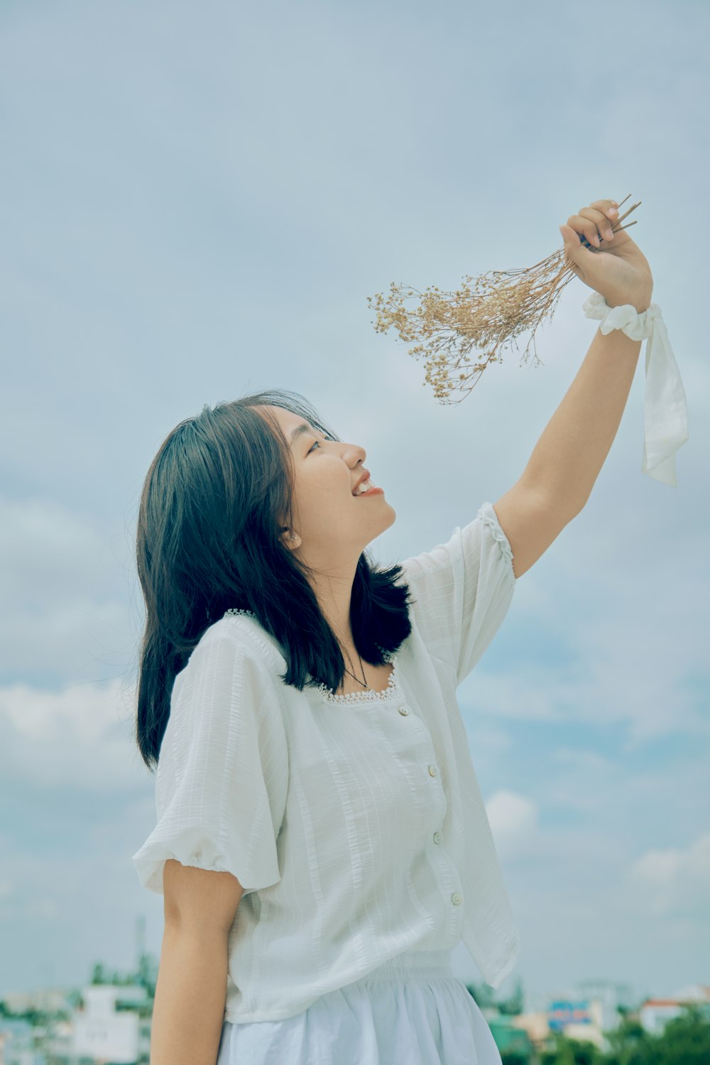woman in white long sleeve shirt holding white flower under white clouds during daytime