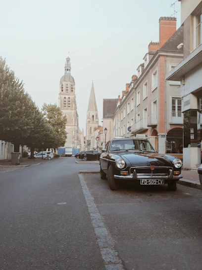 A classic European vintage car parked on a quiet cobblestone street with muted cream and deep brown tones.